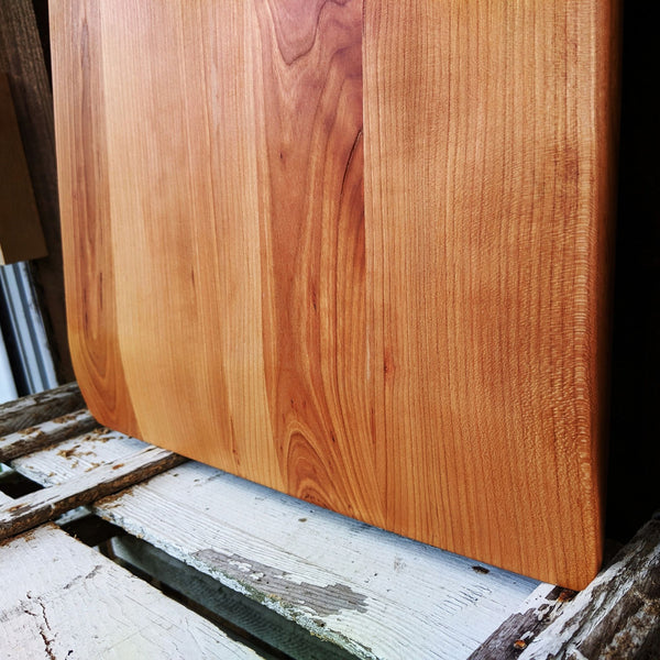 Cherry Wood charcuterie board with handle leaning against backdrop