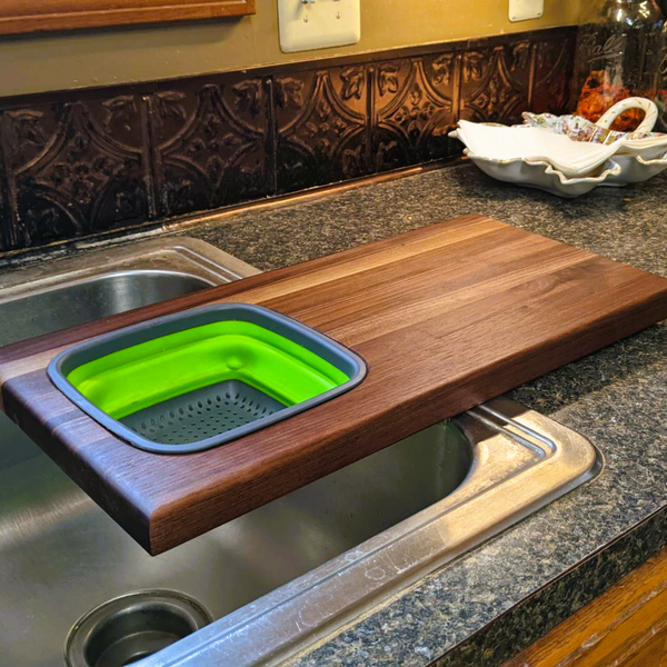 Over the sink Black Walnut edge grain cutting board with removable colander / strainer and clear rubber grip feet.