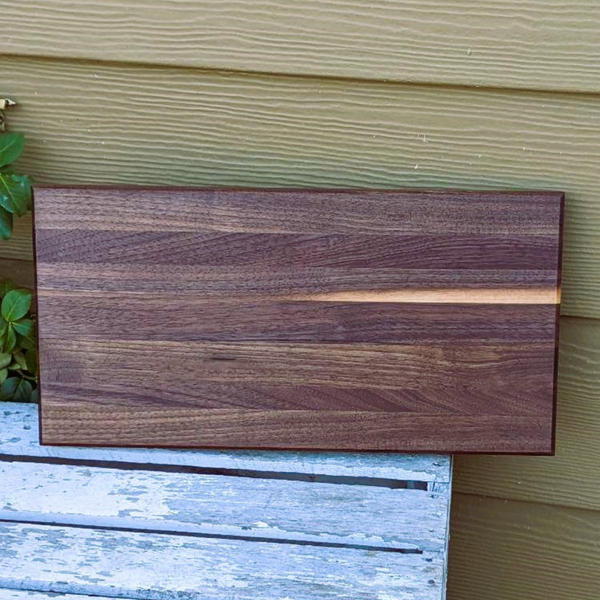 Black walnut wood edge grain cutting board with beveled edge.