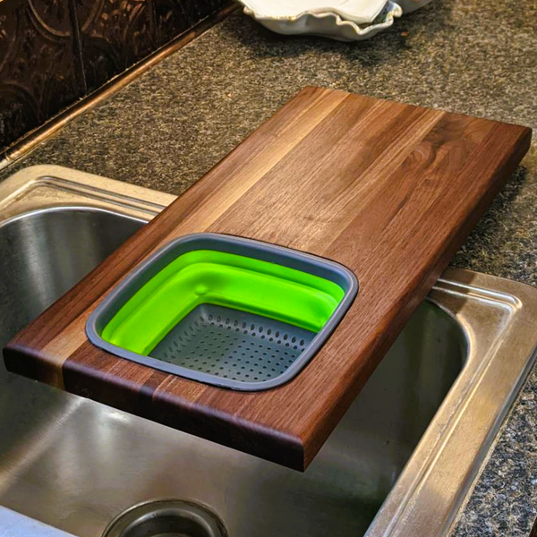 Over the sink Black Walnut edge grain cutting board with removable colander / strainer and clear rubber grip feet.