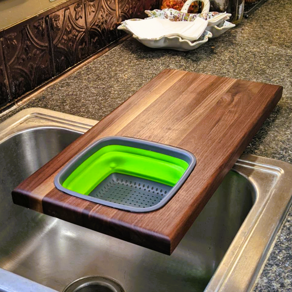 Over the sink Black Walnut edge grain cutting board with removable colander / strainer and clear rubber grip feet.