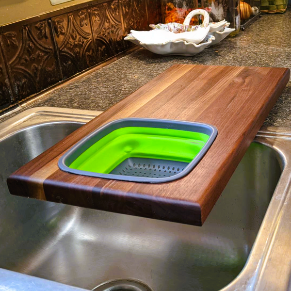 Over the sink Black Walnut edge grain cutting board with removable colander / strainer and clear rubber grip feet.