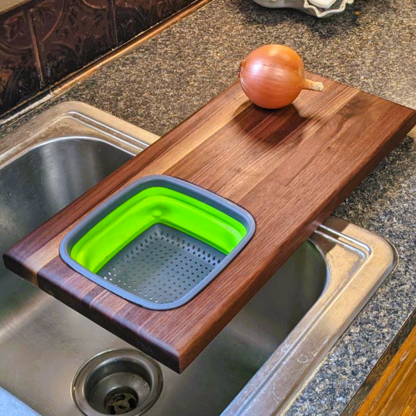 Over the sink Black Walnut edge grain cutting board with removable colander / strainer and clear rubber grip feet.