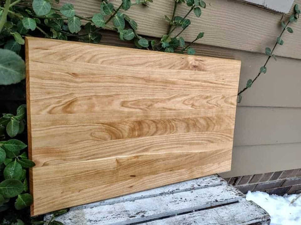 Cherry Wood edge grain cutting board with hand grooves and clear rubber grip feet.
