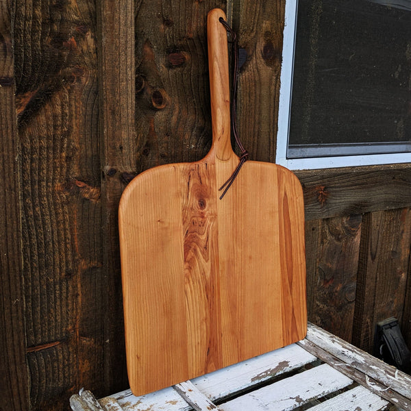 Angled front view of handmade cherry pizza peel against rustic wood wall