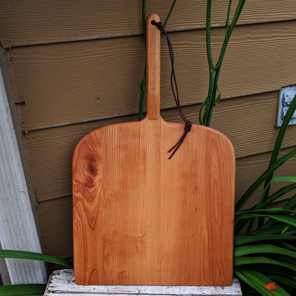 Cherry Wood charcuterie board with handle leaning against backdrop