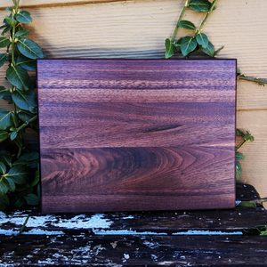 Front view of black walnut edge grain cutting board with hand grooves and beveled edge