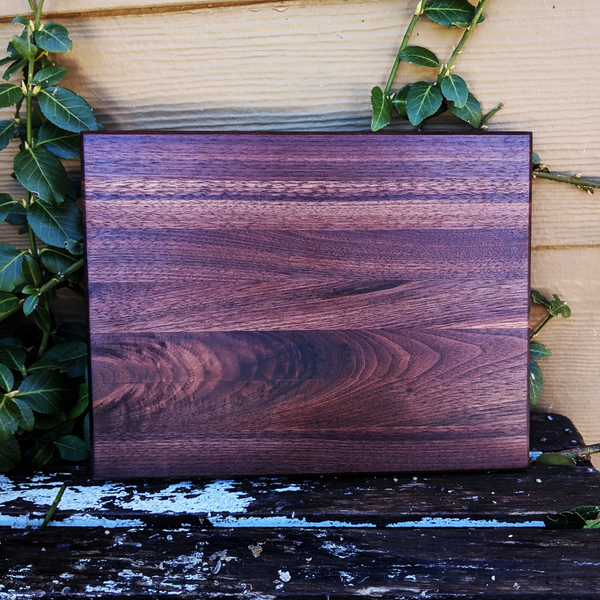 Front view of black walnut edge grain cutting board with hand grooves and beveled edge