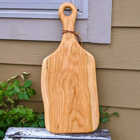 Cherry wood wooden charcuterie paddle serving board with handle and leather strap.