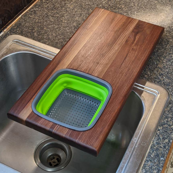 Over the sink Black Walnut edge grain cutting board with removable colander / strainer and clear rubber grip feet.