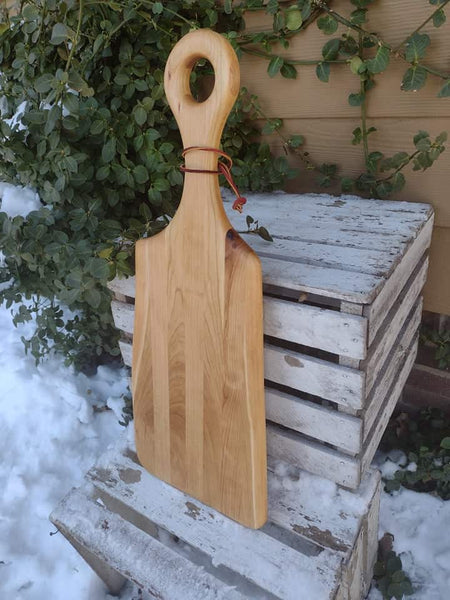 Handmade Cherry Wood charcuterie board paddle with handle and leather strap for easy storage options.