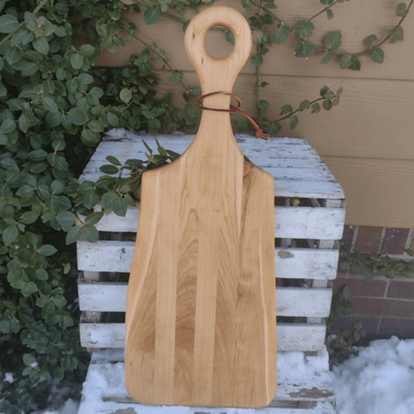 Handmade Cherry Wood charcuterie board paddle with handle and leather strap for easy storage options.