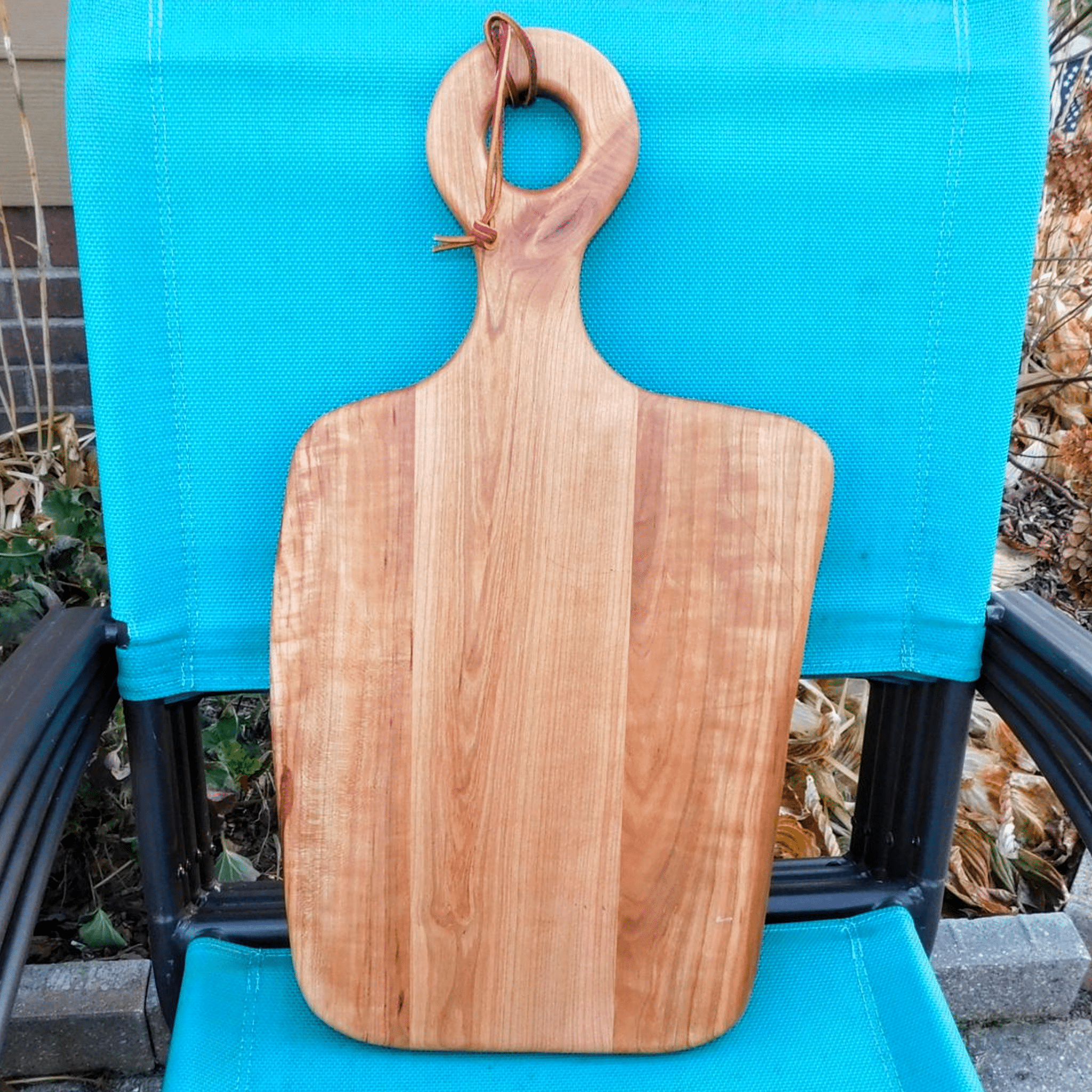 Cherry Wood charcuterie board with handle and leather strap for easy handling and storage options.