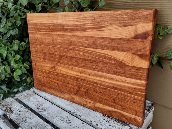 Cherry Wood edge grain cutting board with hand grooves on bottom sides and beveled edge.