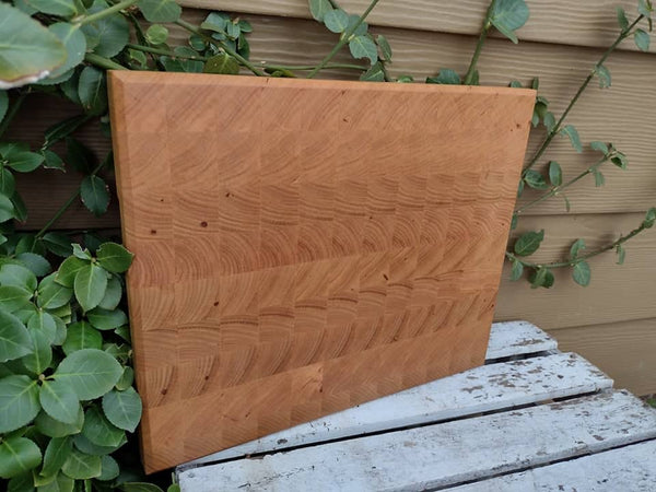 End grain Chery Wood cutting board with beveled edge and clear rubber grip feet.