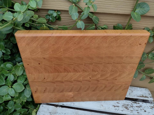 End grain Chery Wood cutting board with beveled edge and clear rubber grip feet.