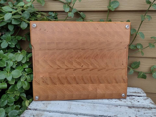 End grain Chery Wood cutting board with beveled edge and clear rubber grip feet.